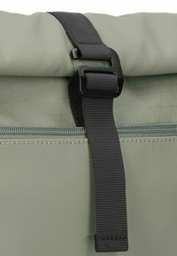 Borsa verde realizzata in materiale testurizzato, con una cintura nera a fibbia e una chiusura con zip sulla parte superiore. Dettagli di cucitura geometrica sottili.