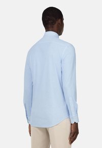 Camisa de manga larga azul claro con cuello abotonado, hecha de tela suave. Presenta puños de un botón y un dobladillo curvado.