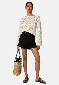 Vit stickad tröja med strukturerat diamantmönster, svarta denimshorts och en vävd toteväska. Svarta sandaler med minimalistisk design.