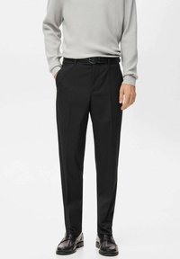 Mężczyzna w czarnych dopasowanych spodniach z kieszeniami po bokach, czarnym pasku, szarym prążkowanym swetrze z długim rękawem oraz czarnych skórzanych mokasynach na białym tle.