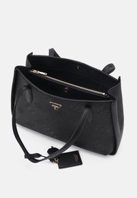 Sac cabas en cuir noir avec motifs embossés, deux poignées et une ouverture supérieure révélant une poche intérieure zippée et une petite étiquette attachée.