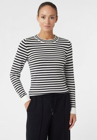 Maglione a righe bianche e nere con maniche lunghe e scollatura rotonda, abbinato a pantaloni neri dalla vestibilità comoda.