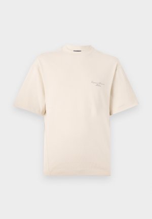 T-shirt beige à manches courtes avec col rond, fabriqué en tissu coton doux. Présente un texte brodé subtil sur le côté gauche du devant.