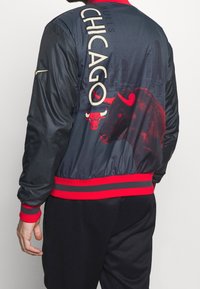 Chicago Bulls varsity jakke med sort stof, røde detaljer, grafisk tyrekæde logo og byens skyline-design på ryggen.