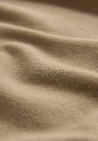 Beige Stoff mit einer weichen Textur, der subtile Rillen und eine glatte Oberfläche zeigt, geeignet für Bekleidungs- oder Polsteranwendungen.