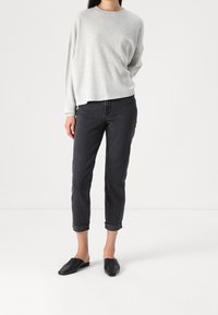 Un maglione a coste grigio chiaro, jeans neri cropped con risvolti e scarpe slip-on nere creano un outfit casual in monocromo.