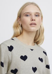 Maglione grigio con motivi a cuore navy, scollatura a girocollo a costine e maniche lunghe. Tessuto morbido, vestibilità casual.