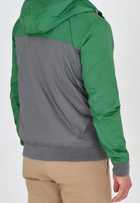 Zielona i szara kurtka z kapturem z elastycznymi mankietami, gładką teksturą i kontrastowym wzorem na plecach. Posiada ściągacz na dolnym brzegu i lekki materiał.