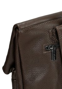 Bruine leren tas met een gestructureerde afwerking, voorzien van een rits en een metalen label met "wojas." Vlotte randen en een gevouwen klep ontwerp.