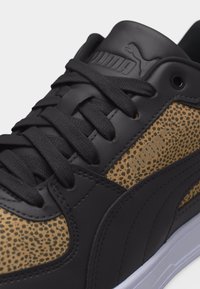 Κοντινό πλάνο μαύρου αθλητικού παπουτσιού με καφέ πάνελ με υφή λεοπάρδαλης, μαύρα κορδόνια και λευκή σόλα.