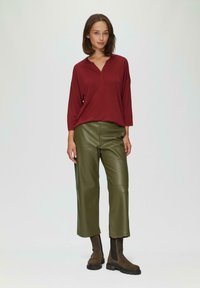 Bordeaux pullover met een kraag, ontspannen pasvorm, gecombineerd met olijfgroene neplederen wijde broek en bruine enkellaarsjes met zwarte zolen.