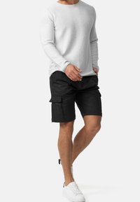 Hellgraues Langarmshirt mit Rundhalsausschnitt, kombiniert mit schwarzen Cargo-Shorts mit seitlichen Taschen und einer lockeren Passform, abgerundet mit weißen Sneakern.