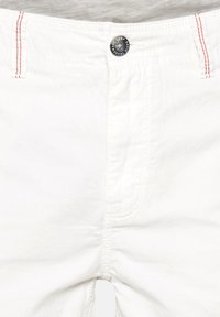 Pantaloni albi din bumbac cu închidere frontală cu buton. Au cusături roșii și un buton negru cu marcaj, punând accent pe un design curat și casual.