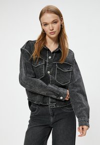 Svart denimjacka med vit kontrastsöm, två bröstfickor, oversized design och knäppningar, i kombination med matchande denimbyxor.