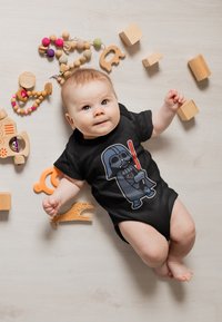 Černá overal s kresleným Darth Vaderem a  červeným světelným mečem. Kolem se nacházejí dřevěné hračky v podobě bloků a korálků v různých barvách a strukturách.