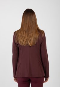 Blazer fitted marrone con maniche lunghe, spalle strutturate e cuciture posteriori sartoriali. Tessuto liscia e linee pulite offrono una silhouette elegante.
