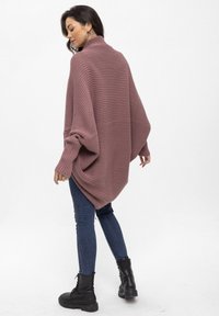 Übergroßer, mauvefarbener Strickpullover mit geripptem Muster, hohem Kragen und fallen Schultern, kombiniert mit schmalen blauen Jeans und schwarzen Kampfstiefeln.
