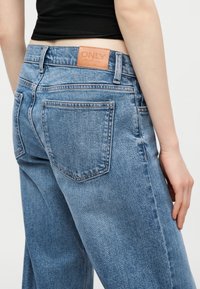 Osoba nosząca wysokie niebieskie dżinsy marki "ONLY" z skórzaną metką oraz czarny krótki top, z ręką opartą przy boku.