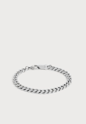 Bracelet chaîne en métal ton argenté avec un fermoir mousqueton sécurisé gravé du nom de la marque "Guess" sur fond blanc.