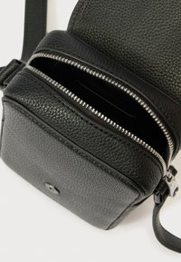 Fekete, texturált bőr keresztpántos táska elülső zsebfedővel és részben nyitott, felső cipzáras rekesszel, fehér háttéren.