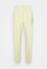 Světle žluté tepláky vyrobené z měkké látky, s elastickým páskem a manžetami u kotníků, s jemným detailem loga na boku.