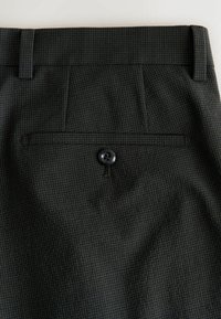 Dunkelgraue Anzughose mit feinem Karo-Muster, mit einer hinteren Leistentasche, die mit einem schwarzen Knopf gesichert ist, und Gürtelschlaufen am Bund.