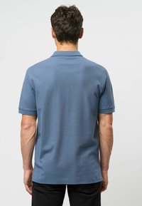 Pánská polo košile s krátkým rukávem v světle modré barvě, žebrovaná textura, s límečkem a detailním švem na zadní části; nošena s tmavými kalhotami.