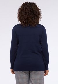 Suéter de punto azul marino con textura de rayas horizontales, mangas largas y dobladillo ajustado, combinado con pantalones de cuadros.