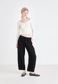 Top corto a maniche lunghe di colore crema con texture a coste, pantaloni neri a gamba larga e ballerine nere in rete con borchie. Foulard a fantasia.
