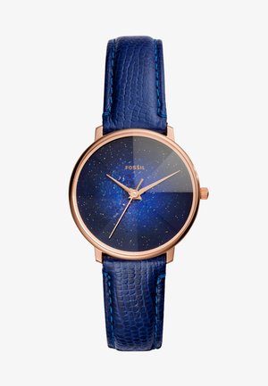Montre ronde en or rose avec cadran bleu ciel étoilé, aiguilles dorées et bracelet en cuir bleu texturé, nom de la marque Fossil visible sur le cadran.