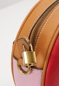 Okrągła torebka z dwu tonowej skóry w kolorach czerwonym i różowym, z wyrazistym złotym zamkiem błyskawicznym i detalem w postaci kłódki, prezentująca gładkie tekstury i kontrastujące kolory.