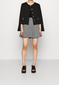 Černá zkrácená bunda se stříbrnými knoflíky, spárovaná s kostkovanou sukní s volánem. Model má na sobě černé masivní podpatky. Minimalistický design.