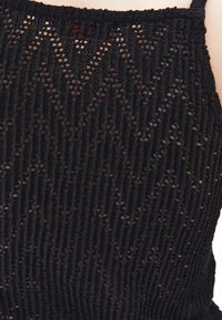 Top nero lavorato a maglia con un motivo a zigzag e una texture semi-trasparente. Spalline sottili e dettagli a coste lungo i bordi.