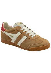 Sneaker in suede marrone con strisce bianche, accento rosso sul tallone e suola in gomma testurizzata. Presentano lacci e branding dorato sulla linguetta.