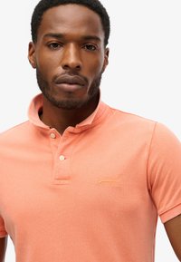 Korte mouw polo shirt in licht koraal met een gestructureerde stof, een kraag en een klein geborduurd logo in geel.