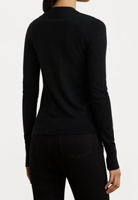 Svart långärmad tröja, rund halsringning, mjukt stickat material, figurnära siluett, med ribbade ärmslut och nederkant, bärs över mörka jeans.