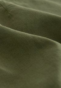 Olive green fabric showing textured surface with visible weave patterns, featuring soft drapes and subtle variations in color intensity.