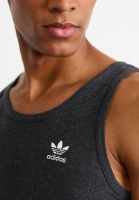 Geribbelde antracietkleurige tanktop met een ronde halslijn en een wit geborduurd Adidas-logo op de linkerkant van de borst. Zachte stof met een aansluitend ontwerp.