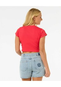 Top corto a righe rosse con maniche corte, abbinato a pantaloni shorts in denim azzurro con un dettaglio di ricamo floreale sulla tasca posteriore.