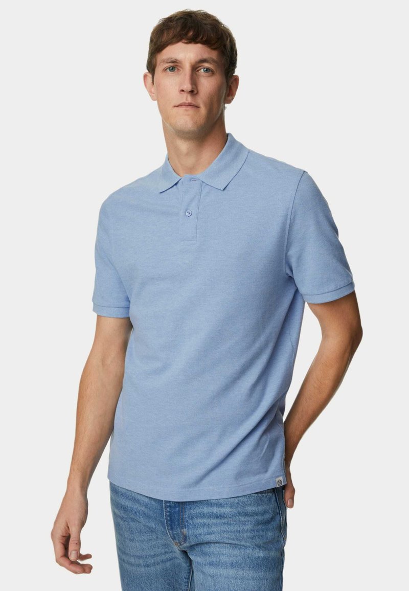 Himmelblaues Baumwoll-Polo-Shirt mit einem kurzen Kragen, zwei Knöpfen und umgeschlagenen Ärmeln, kombiniert mit blauen Jeans.