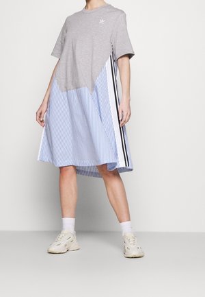 Kvinde iført en afslappet kjole med en grå top og blå- og hvidstripet nederdel, kombineret med hvide sokker og chunky hvide sneakers.