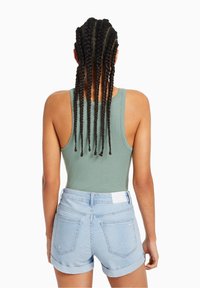 Top sin mangas verde acanalado combinado con pantalones cortos de mezclilla azul claro, con dobladillos enrollados y una etiqueta blanca en la cintura.