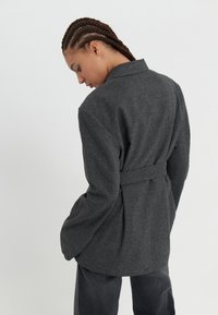 Grå rutete blazer med innsvingt midje og lange ermer, med en påsatt krage og myk, teksturert stoff.