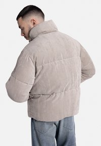 Lichtbeige corduroy pufferjack met een hoge kraag en verticale ribbelstructuur, voorzien van een vierkante vorm en een ontspannen pasvorm.