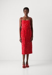 Robe midi rouge avec un corsage structuré, des bretelles délicates et des embellissements en sequins. Associée à des sandales à talons ouverts rouges.