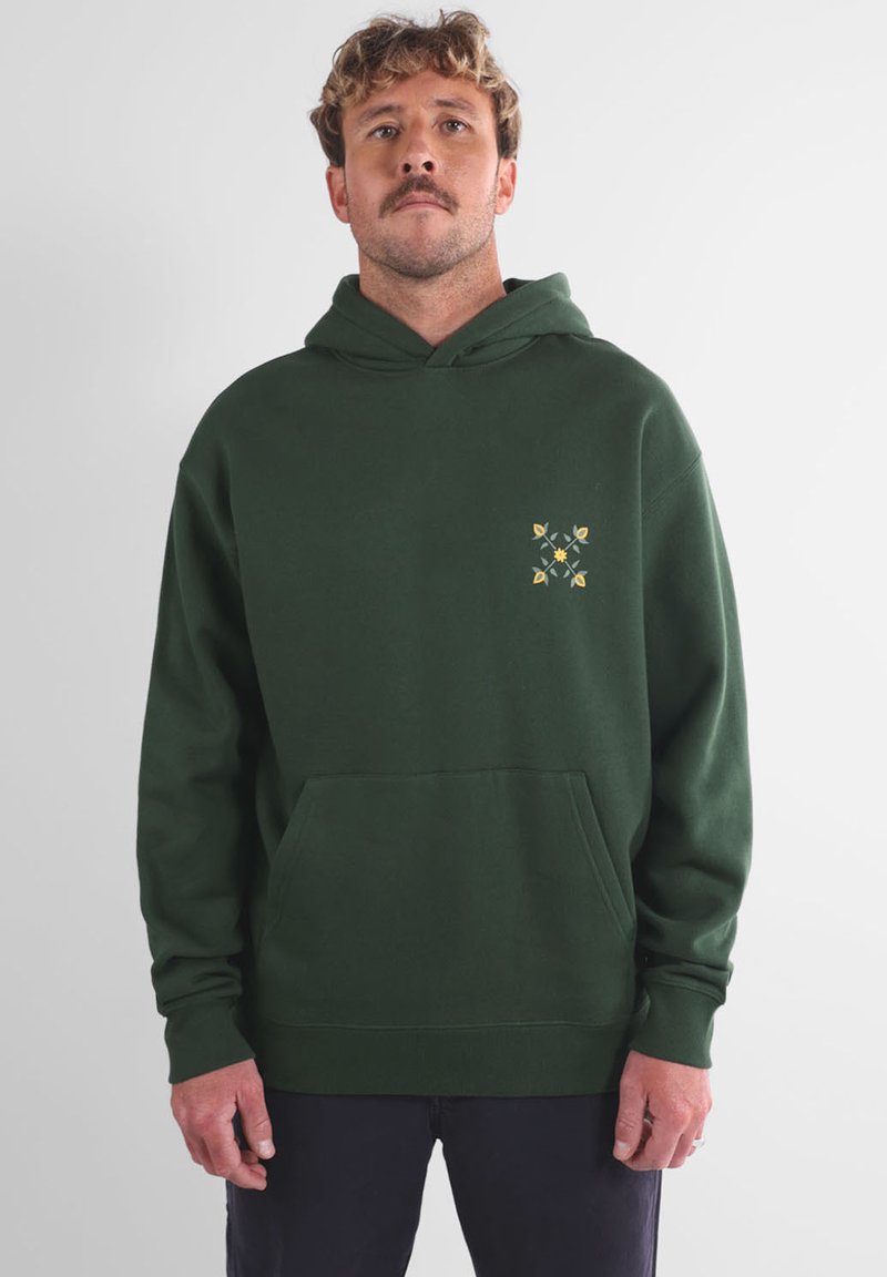 Sweat à capuche vert foncé avec une poche avant et un motif floral jaune et vert sur le côté gauche de la poitrine. Tissu doux et texturé.