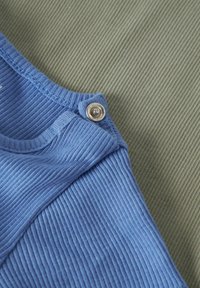 Gros plan sur un tissu bleu côtelé avec un bouton pression argenté à une extrémité, posé sur un fond de tissu côtelé gris-vert texturé.