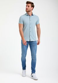 Polo shirt azzurro chiaro a maniche corte con bottoni, abbinato a jeans slim-fit e sneaker bianchi con dettagli neri.