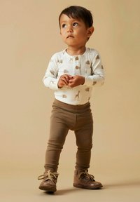 Body z długim rękawem w kolorze kości słoniowej z nadrukami zwierząt i guzikami, w zestawie z brązowymi elastycznymi spodenkami oraz jasnobrązowymi sznurowanymi butami. Gładka tekstura tkaniny.