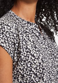 Kortärmad blus i ett vitt och svart abstrakt mönster, med rund halsringning och knapputstyrning fram. Mjuk tygkvalitet.